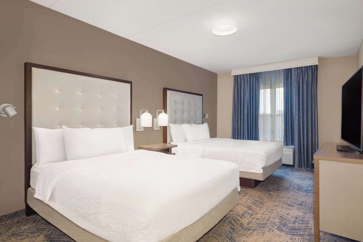 A hotel room with two beds, a TV, and a large window with curtains.