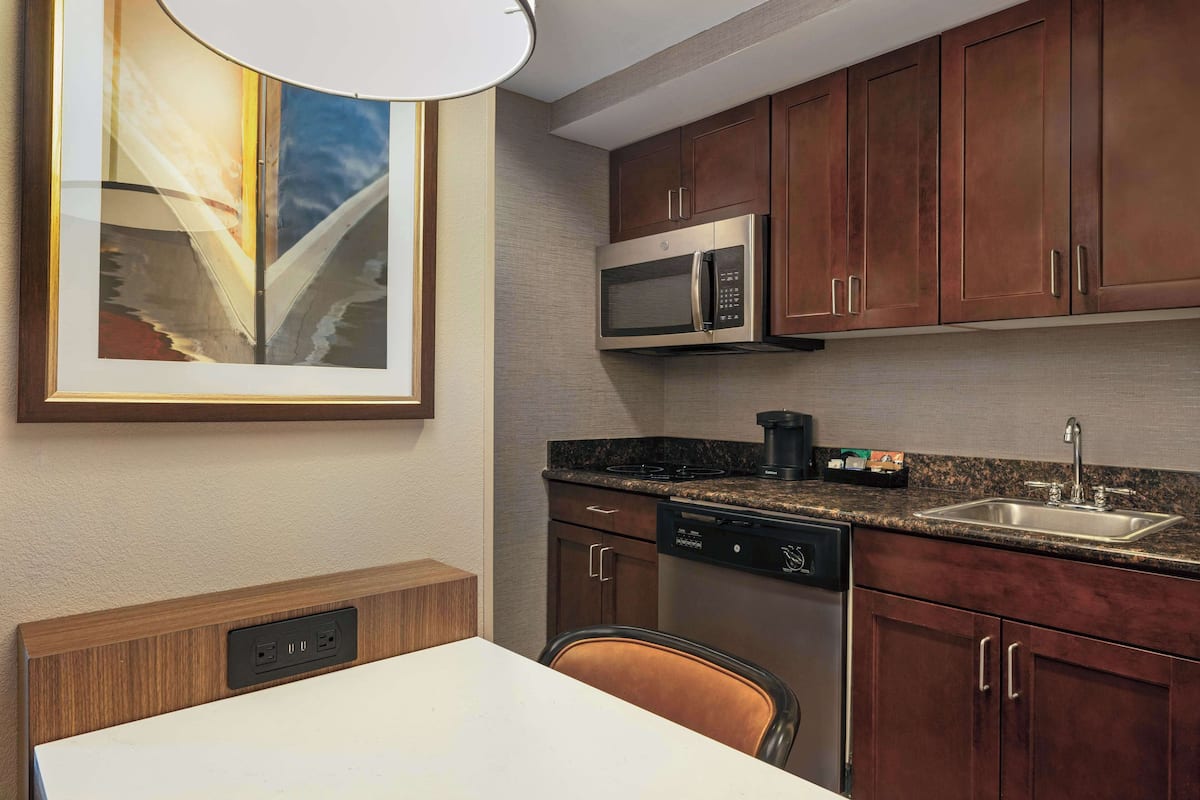 A modern kitchen with dark wooden cabinets, a stainless steel microwave, a dishwasher, and a granite countertop.