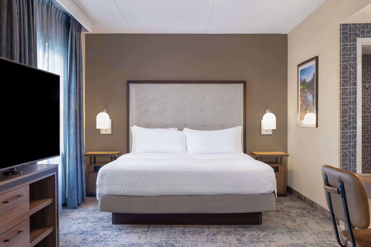 Een hotelkamer met een groot bed, een televisie, een bureau en een stoel.