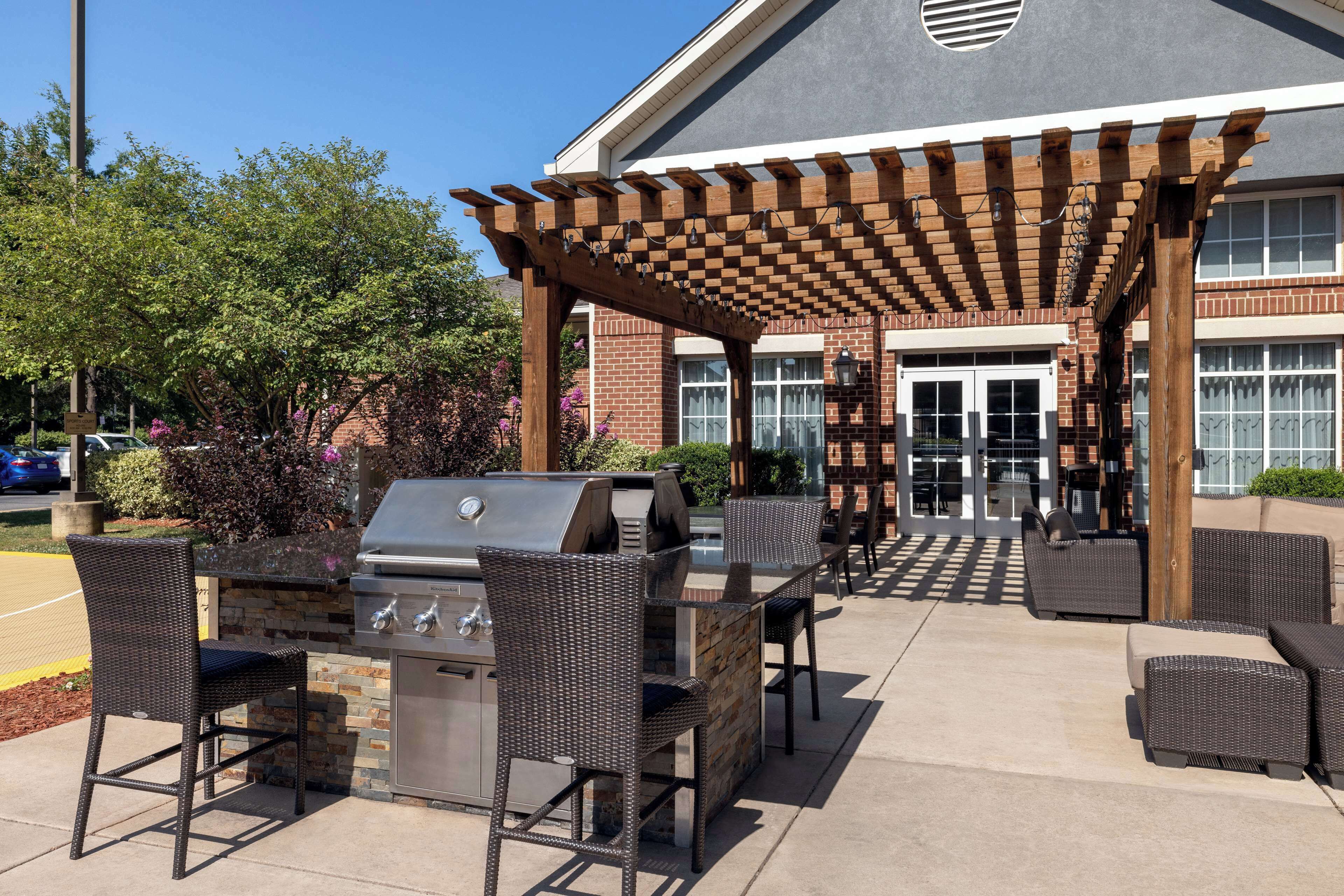 Eine Terrasse im Freien mit Grill, Korbstühlen und einer Pergola.