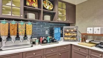 A kitchen area with a coffee station, cereal dispensers, and a display case with pastries.