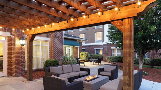 An outdoor patio with wicker furniture, a fire pit, and string lights under a wooden pergola.