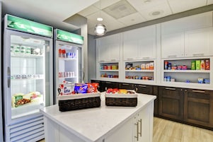 Una cocina equipada con dos refrigeradores llenos de alimentos, una encimera con cestas de aperitivos y alacenas superiores con diversos productos alimenticios.