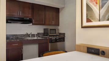 A compact kitchen with dark wooden cabinets, a stainless steel dishwasher, a microwave, and a granite countertop.