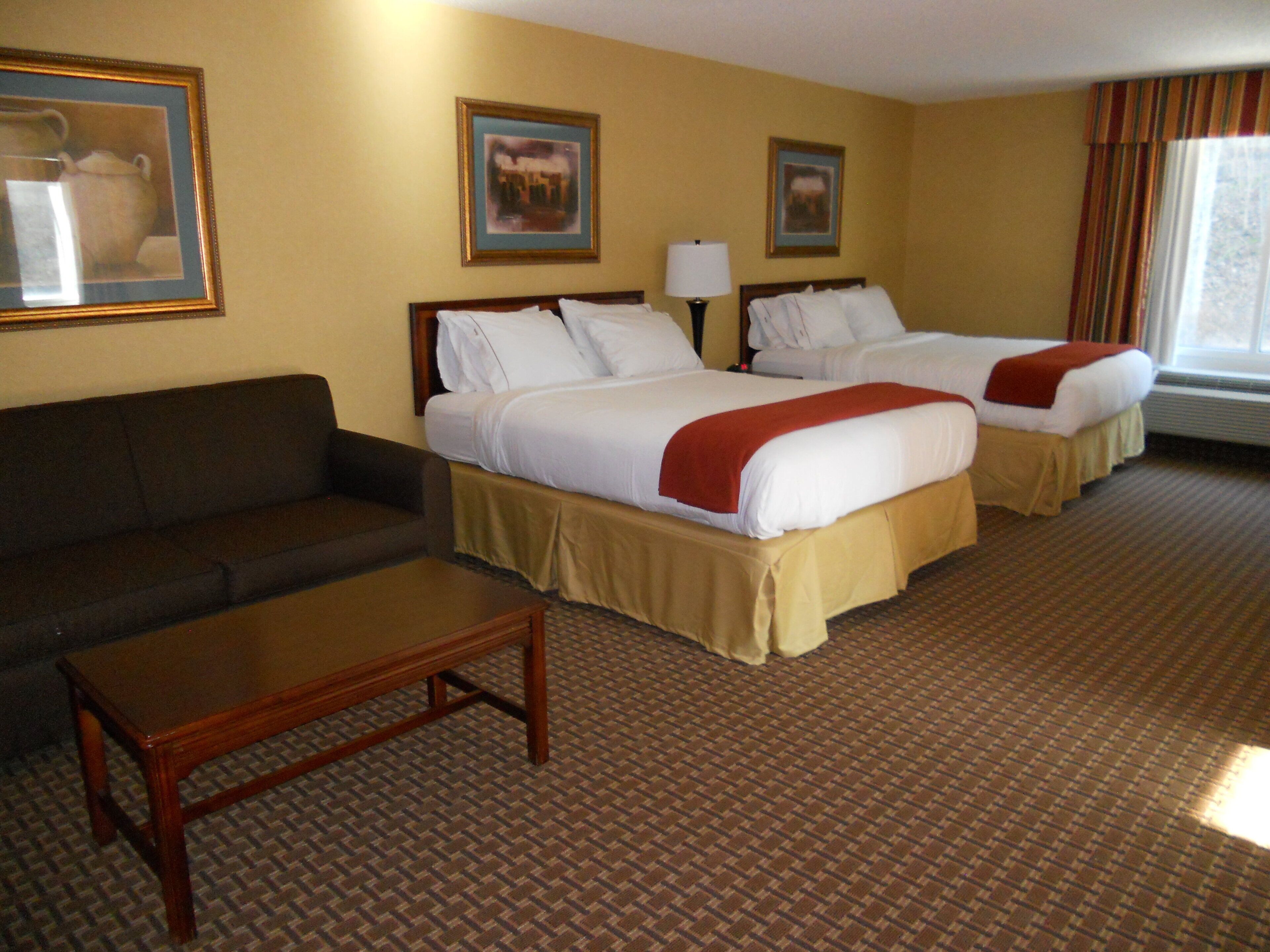 A hotel room with two beds, a sofa, a table, and a window with curtains.