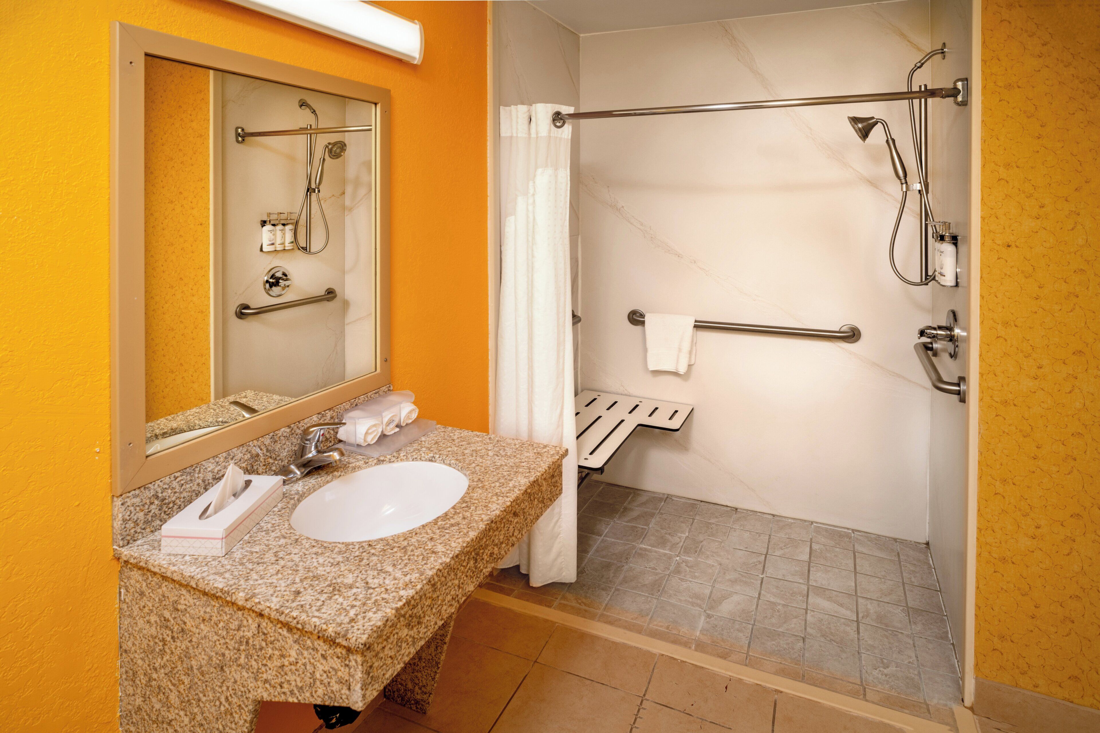 A bathroom with a granite countertop sink, a mirror, a shower with a glass door, and a towel rack.