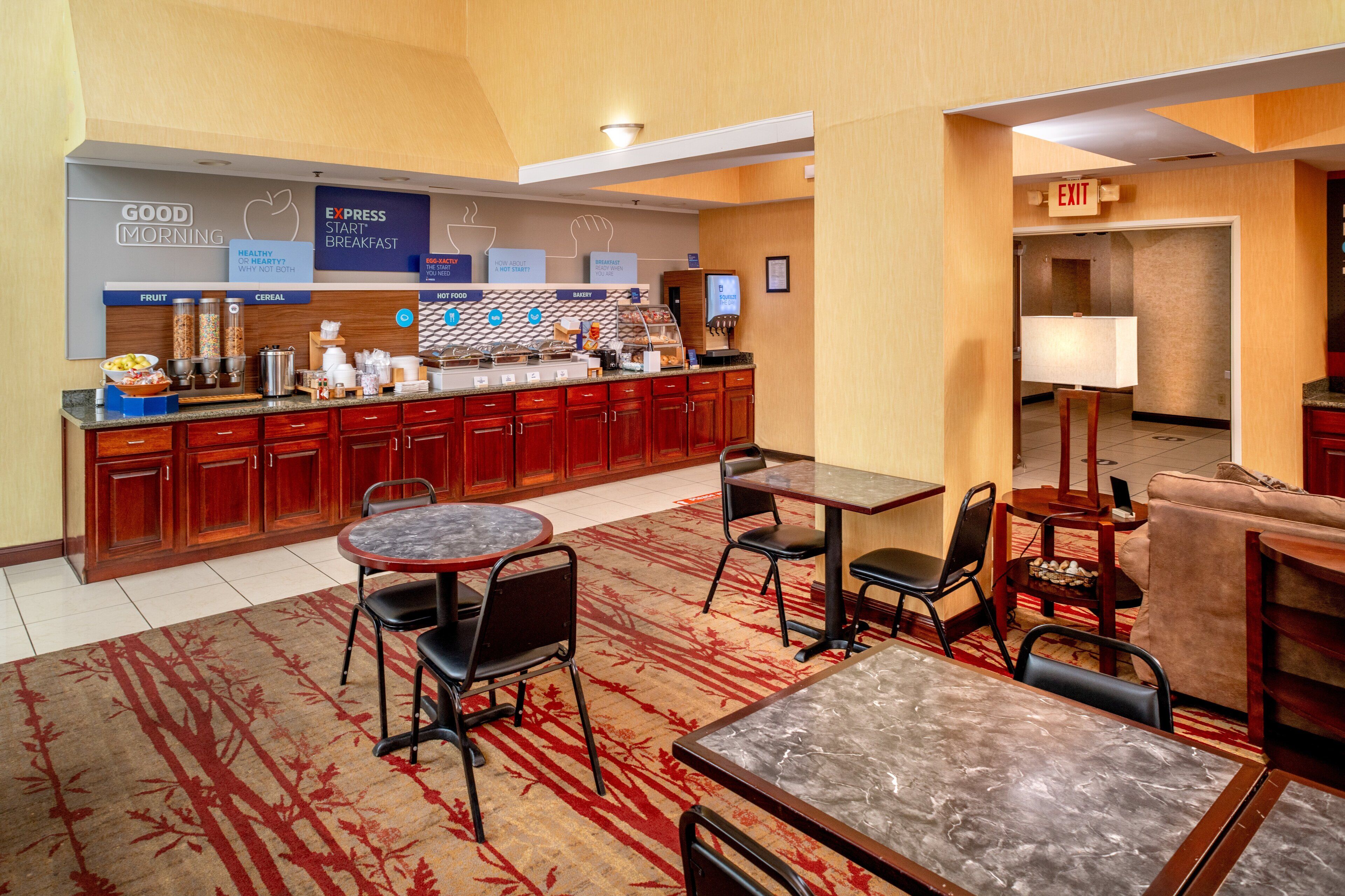 A hotel lobby with a breakfast bar, seating area, and an exit sign.