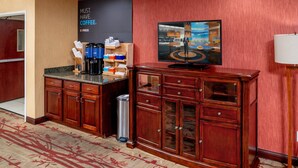 A hotel lobby with a coffee station, a large screen displaying a coffee advertisement, and a wooden cabinet.
