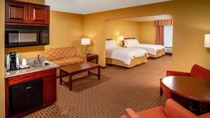 A hotel room with a kitchenette, two beds, a sofa, and a dining table.