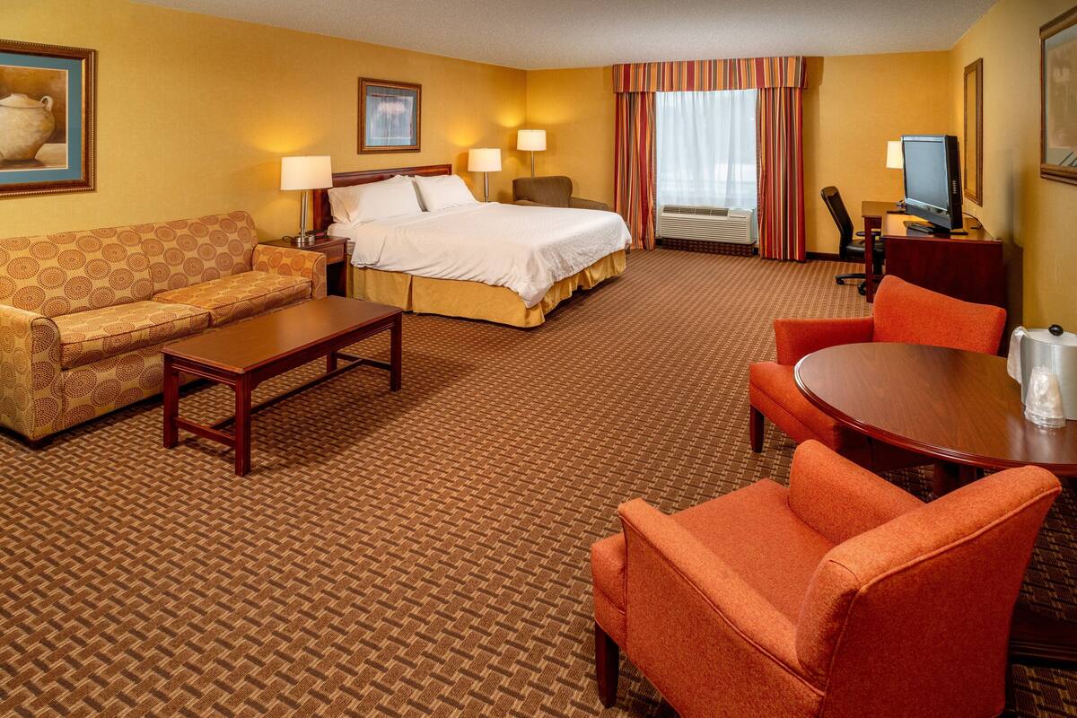 A hotel room with a bed, a sofa, a coffee table, a TV, and a dining table.