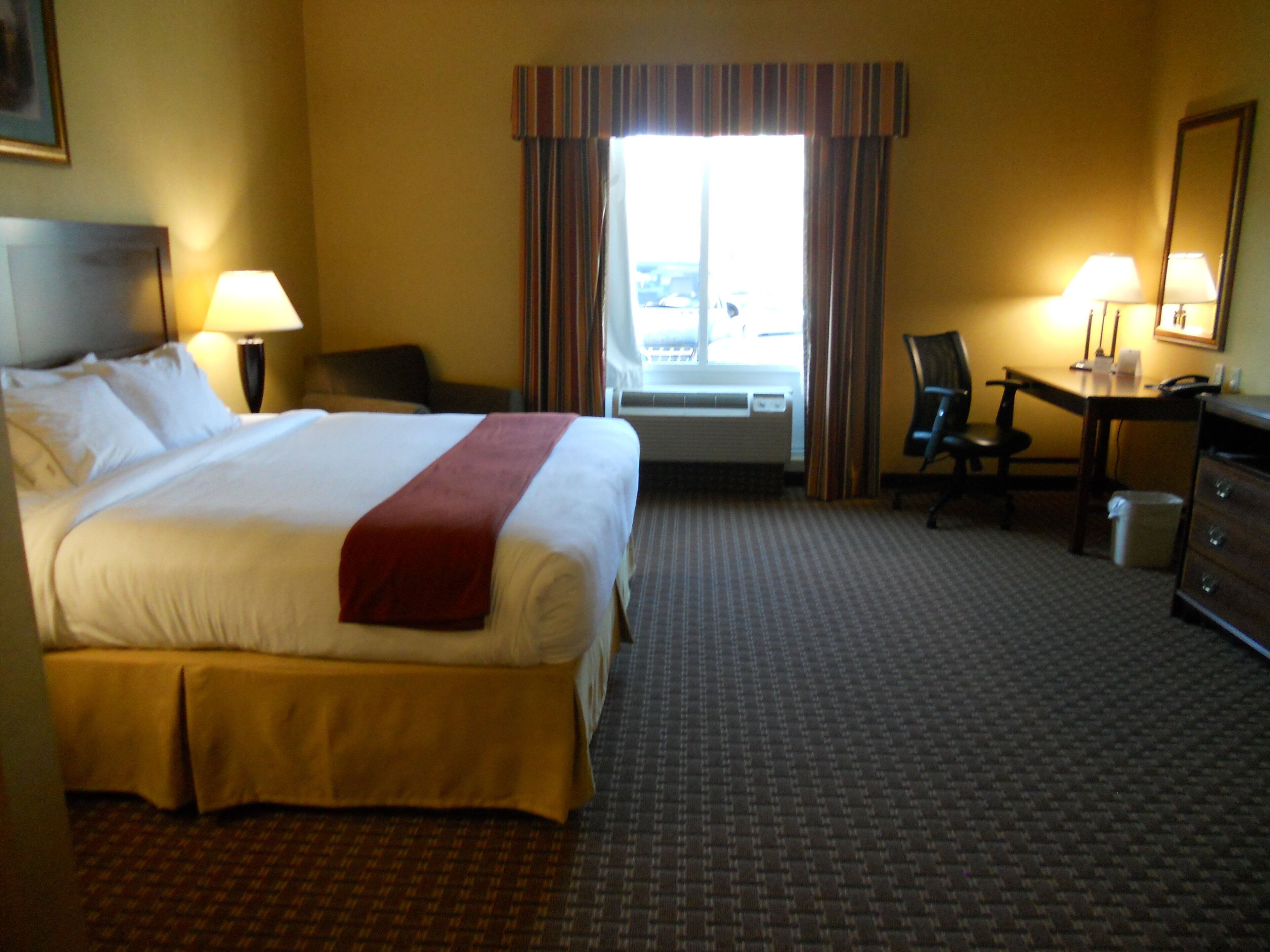 A hotel room with a large bed, a desk, a chair, a lamp, and a window with curtains.