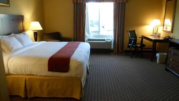 A hotel room with a large bed, a desk, a chair, a lamp, and a window with curtains.