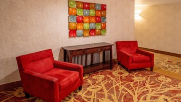A hotel room with two red armchairs, a wooden console table, and a colorful mosaic wall art.