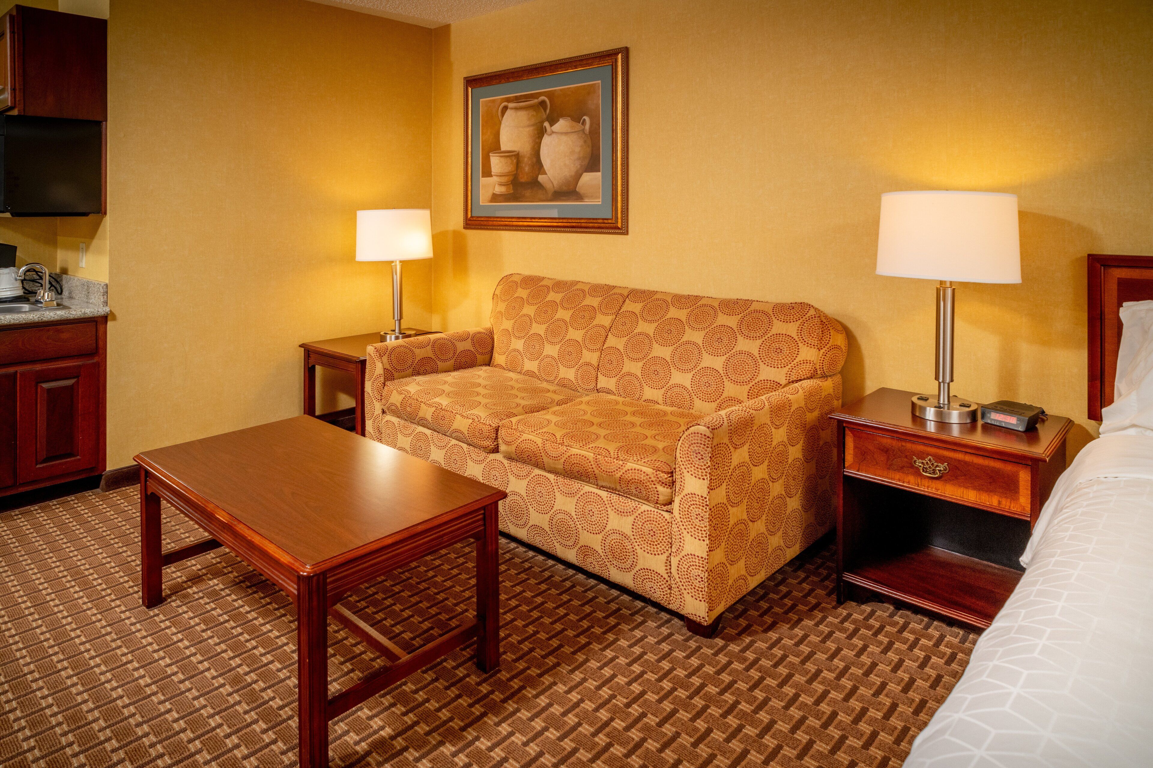 Een hotelkamer met een bank, een houten tafel, een nachtkastje met een lamp en een bed.