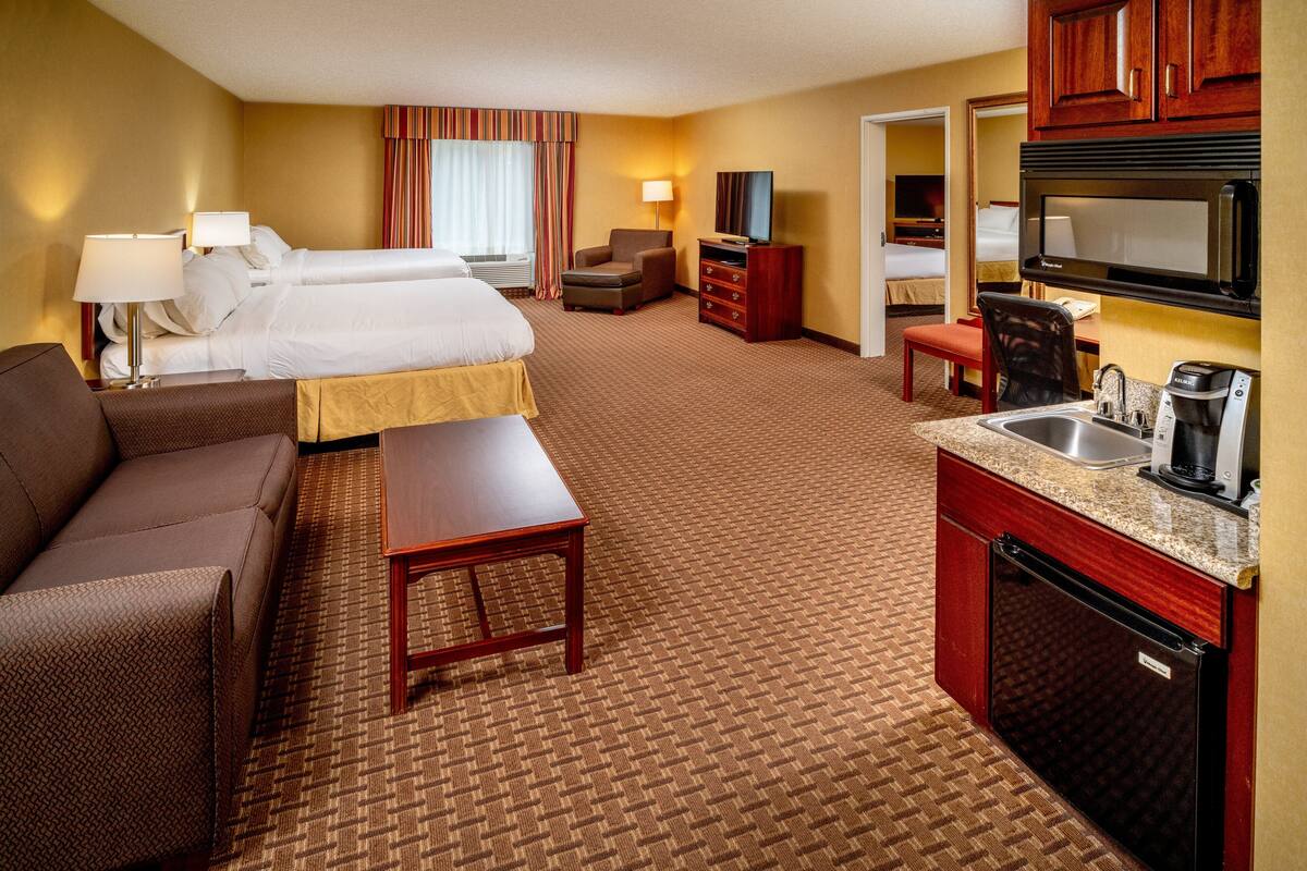 A hotel room with two beds, a sofa, a desk, a coffee maker, a microwave, and a sink.