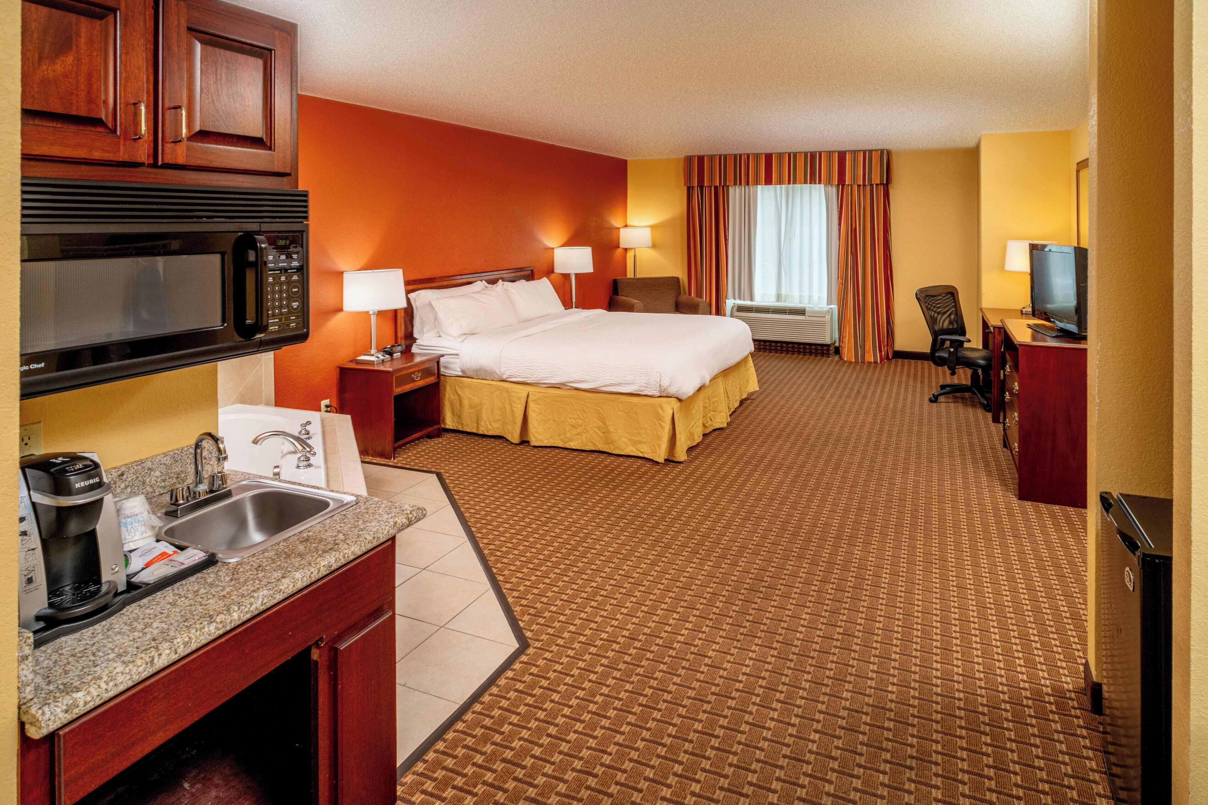 A hotel room with a bed, a desk with a coffee maker, a TV, and a microwave.