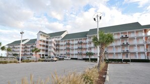 A multi-story hotel with balconies, a parking lot, and a clear sky. - Grand Beach Condominiums by Wyndham Vacation Rentals (Gulf Shores)