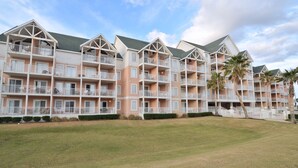 A multi-story hotel with balconies, a well-maintained lawn, and palm trees. - Grand Beach Condominiums by Wyndham Vacation Rentals (Gulf Shores)