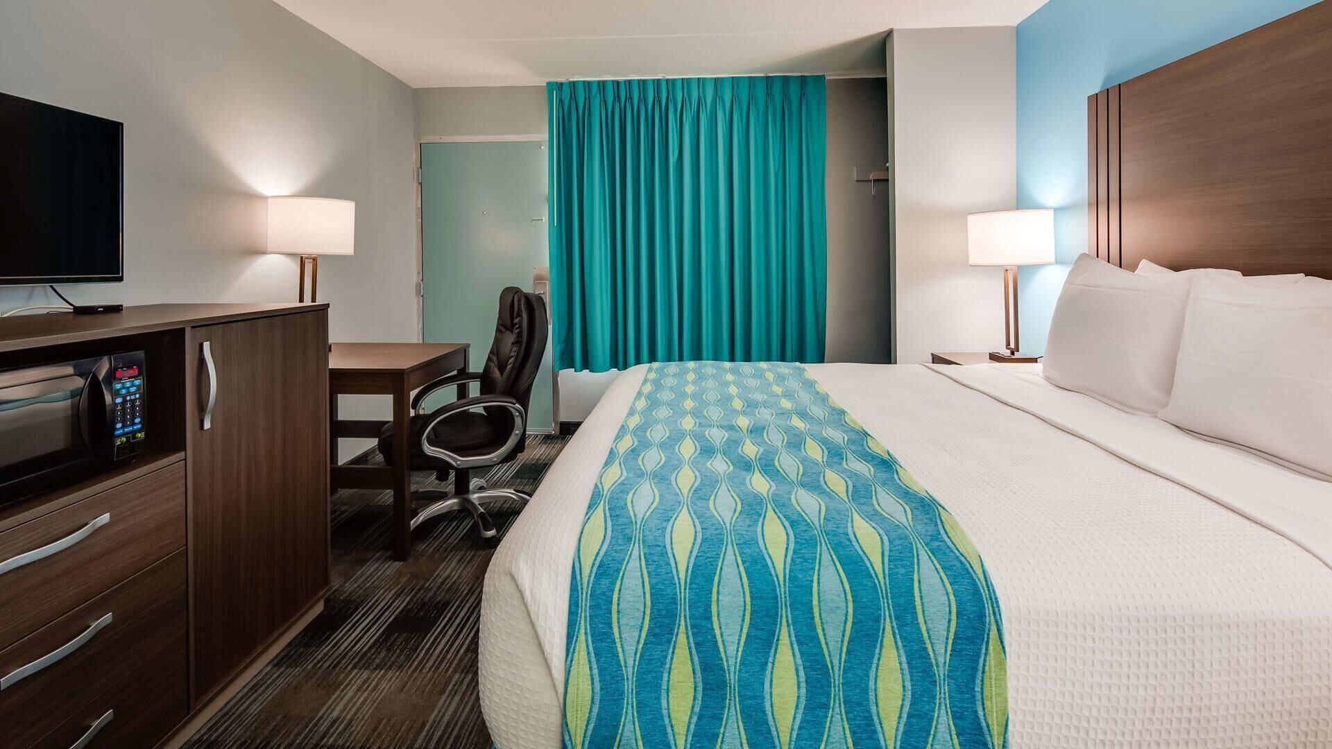 Una habitación de hotel con cama, escritorio, silla, televisor y puerta de baño.