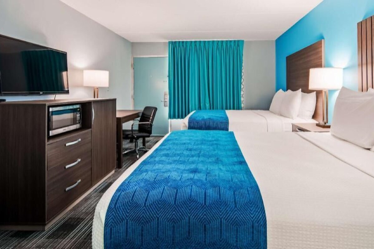 Une chambre d’hôtel avec un lit, un bureau, une télévision et une fenêtre avec des rideaux.