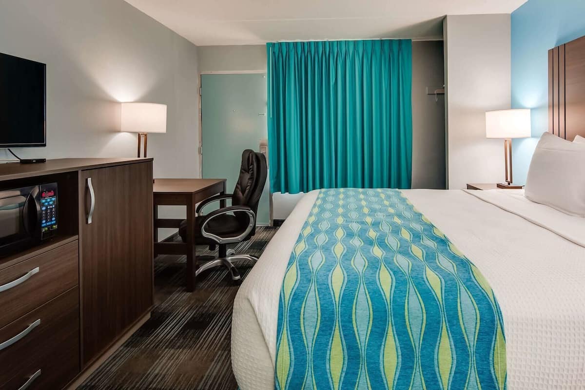 Una habitación de hotel con cama, escritorio, silla, televisor y puerta de baño.