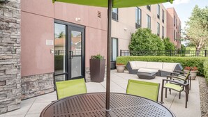 Une terrasse extérieure avec une table ronde, des chaises vertes et un parasol vert.