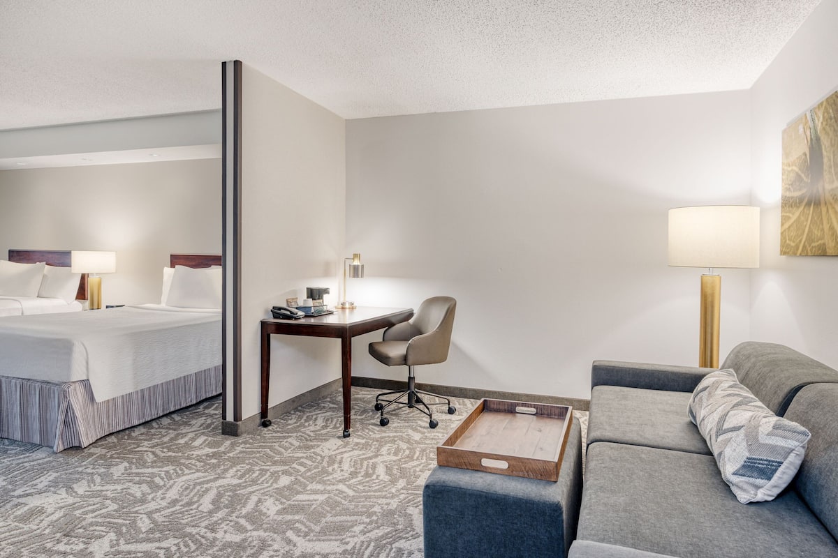 A hotel room with a bed, a desk, a chair, a sofa, and a tray table.