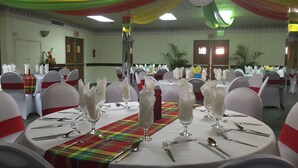 Un salón de banquetes con mesas redondas dispuestas para un evento formal, manteles blancos y cintas rojas en las sillas.