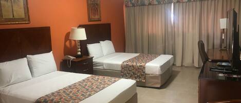 Quarto de hotel com duas camas, uma escrivaninha, uma cadeira, um abajur e uma televisão.