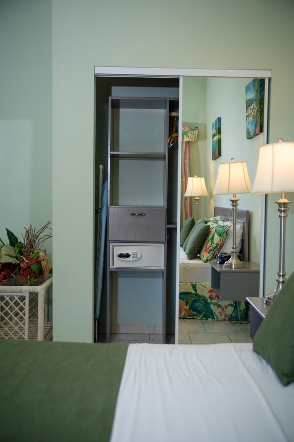 Habitación de hotel con cama, mesita de noche con lámpara, cómoda, espejo y una pequeña mesa con una planta.