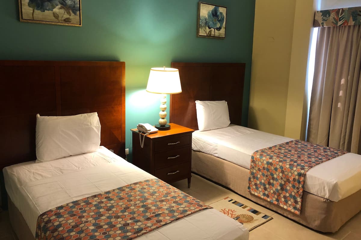 A hotel room with two beds, a nightstand with a lamp, and a small table.
