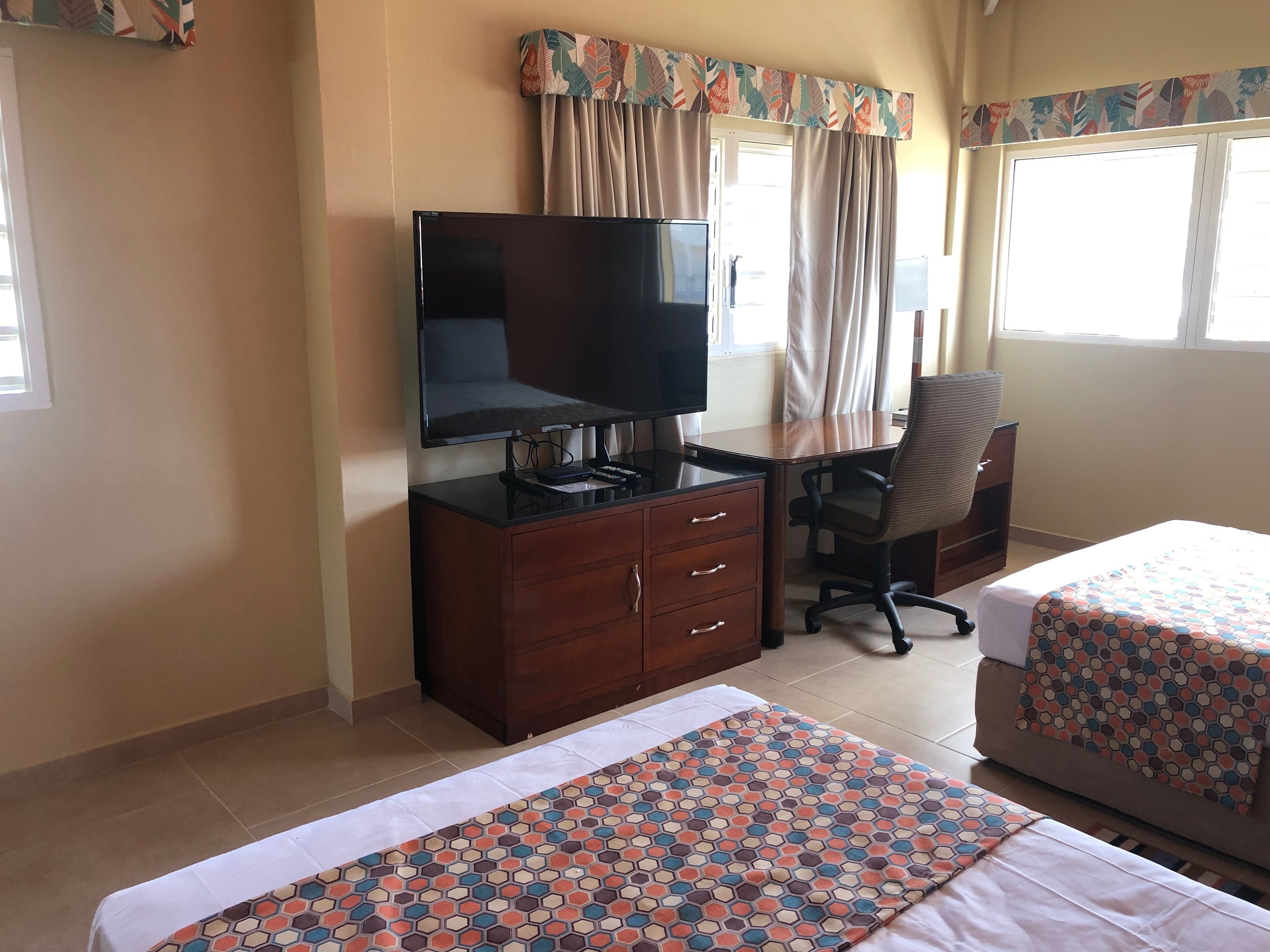 A hotel room with a bed, a desk with a TV, a chair, and a window with curtains.