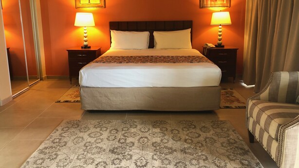 Habitación de hotel con una cama grande, dos mesitas de noche con lámparas, una silla y dos cuadros colgados en la pared.
