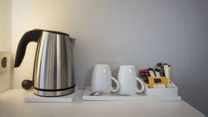 A stainless steel kettle, two white mugs, a spoon, and a tray with chocolate bars and a packet of sugar on a white surface. - Holiday Inn Express Baden-Baden by IHG (Baden-Baden)