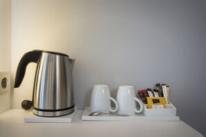 A stainless steel kettle, two white mugs, a spoon, and a tray with chocolate bars and a packet of sugar on a white surface. - Holiday Inn Express Baden-Baden by IHG (Baden-Baden)