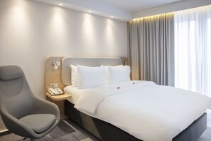 A hotel room with a bed, a chair, a nightstand with a phone, and a window with curtains. - Holiday Inn Express Baden-Baden by IHG (Baden-Baden)