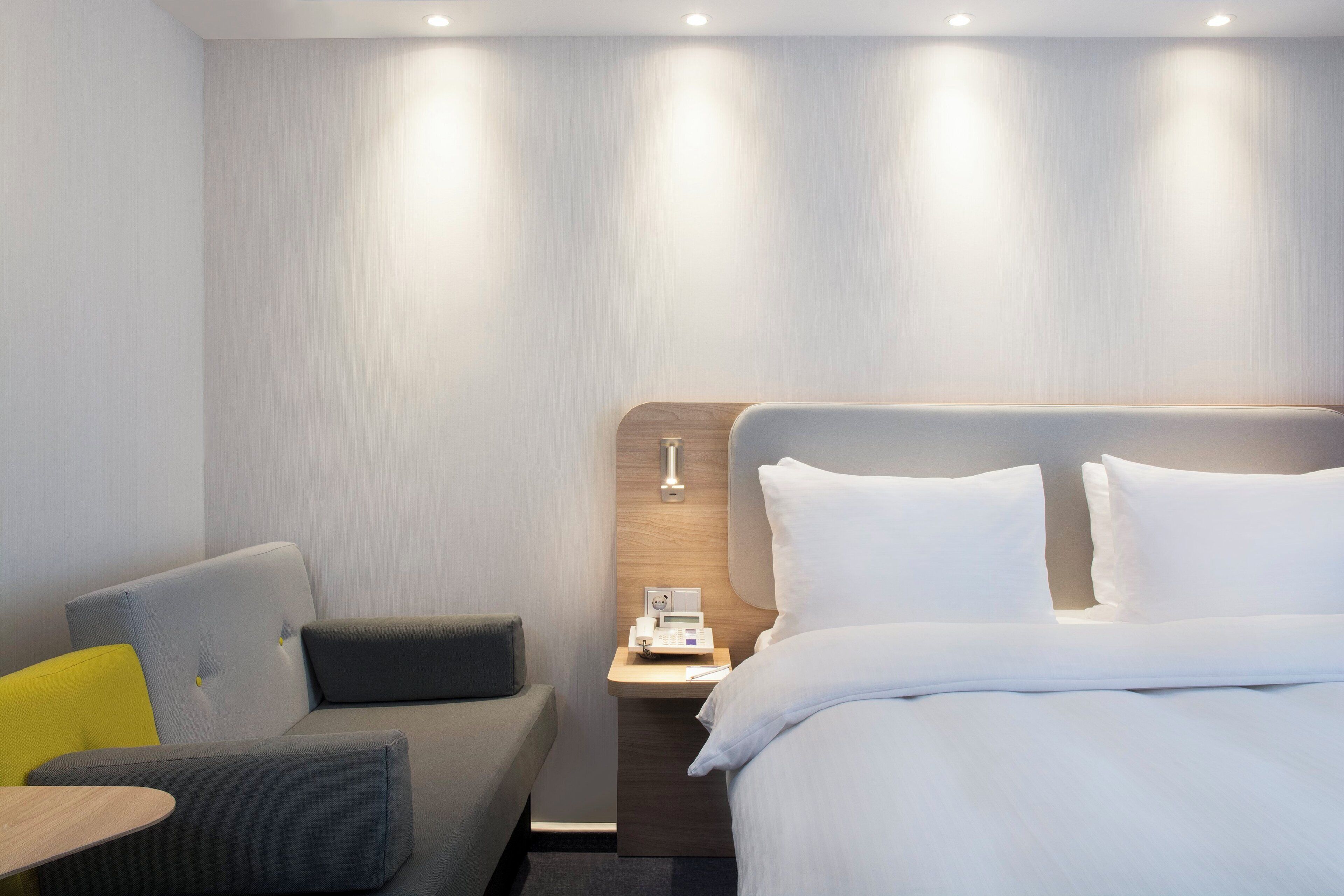A hotel room with a bed, a sofa, a bedside table, and a nightstand.