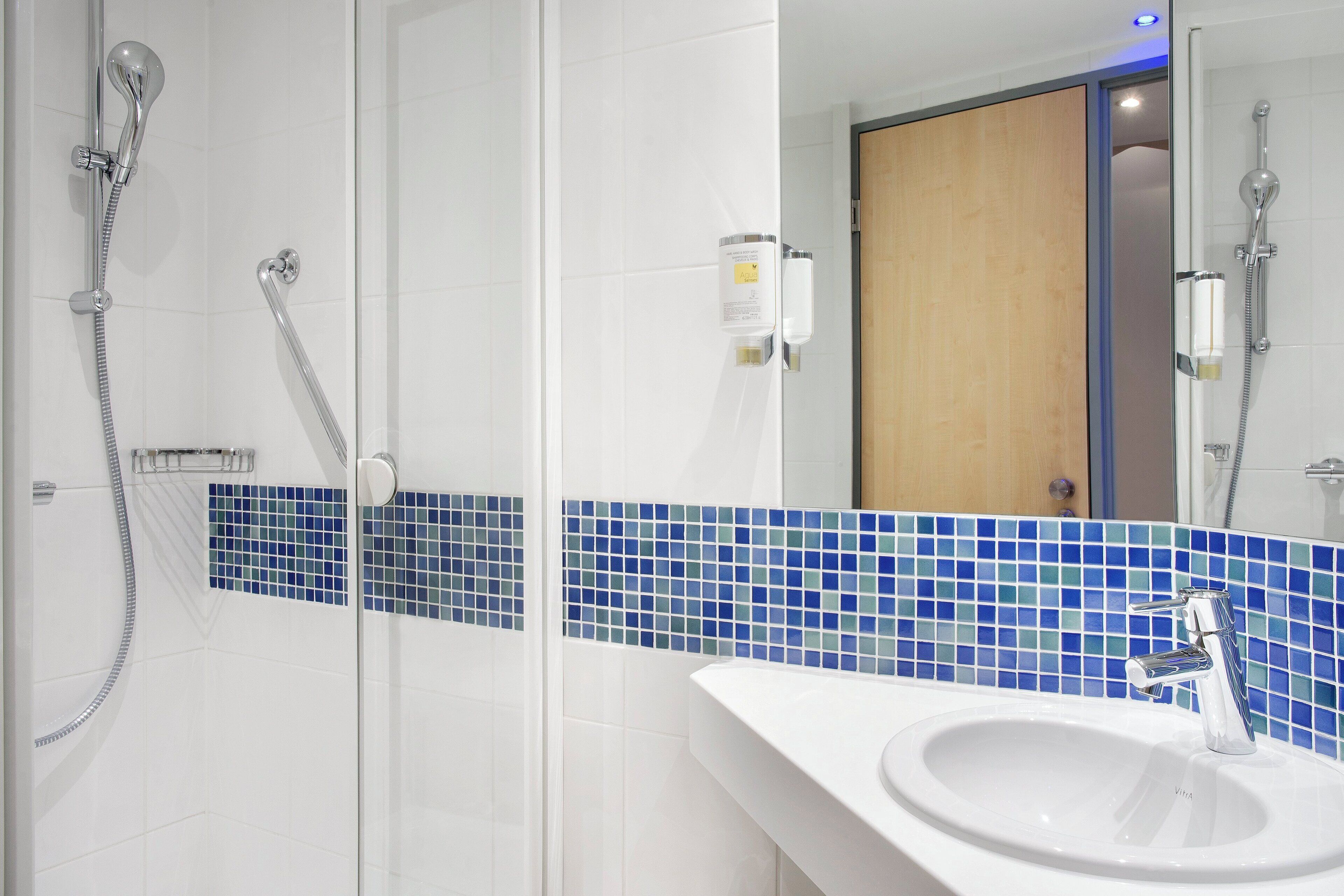 Un baño con lavamanos blanco, un espejo y una ducha con cabezal de ducha manual.