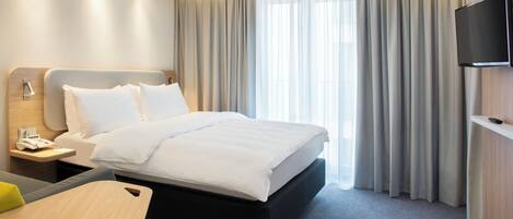 A hotel room with a bed, bedside table, TV, and curtains.