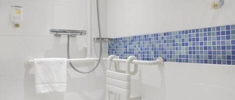 Ein Badezimmer mit weißen Fliesen, einer Wand in blauem Fliesenmuster und weißen Ablageflächen sowie einer weißen Haltestange.