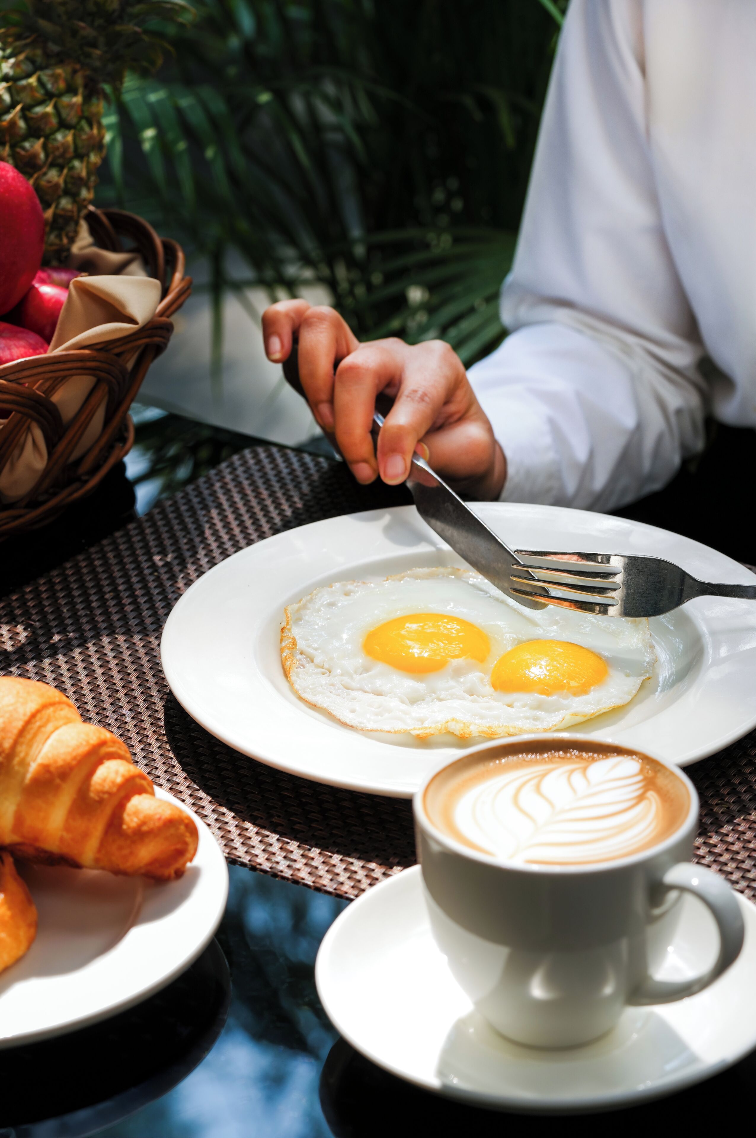 A breakfast setting with eggs, a croissant, and a cup of coffee on a table.