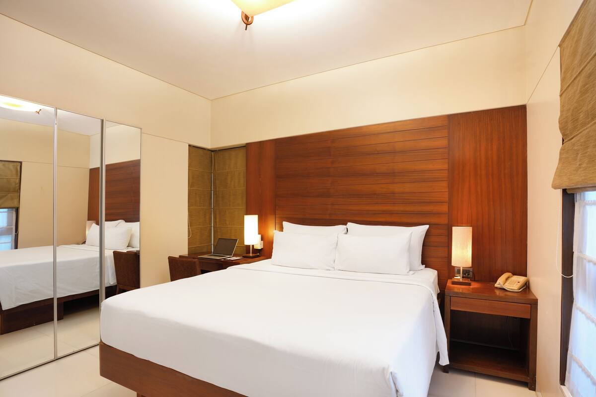A hotel room with a large bed, a bedside table with a lamp, a phone, and a mirror.
