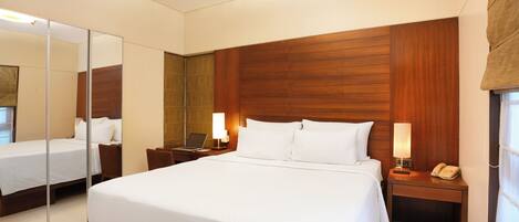 Una habitación de hotel con una cama grande, una mesita de noche con lámpara, teléfono y espejo.