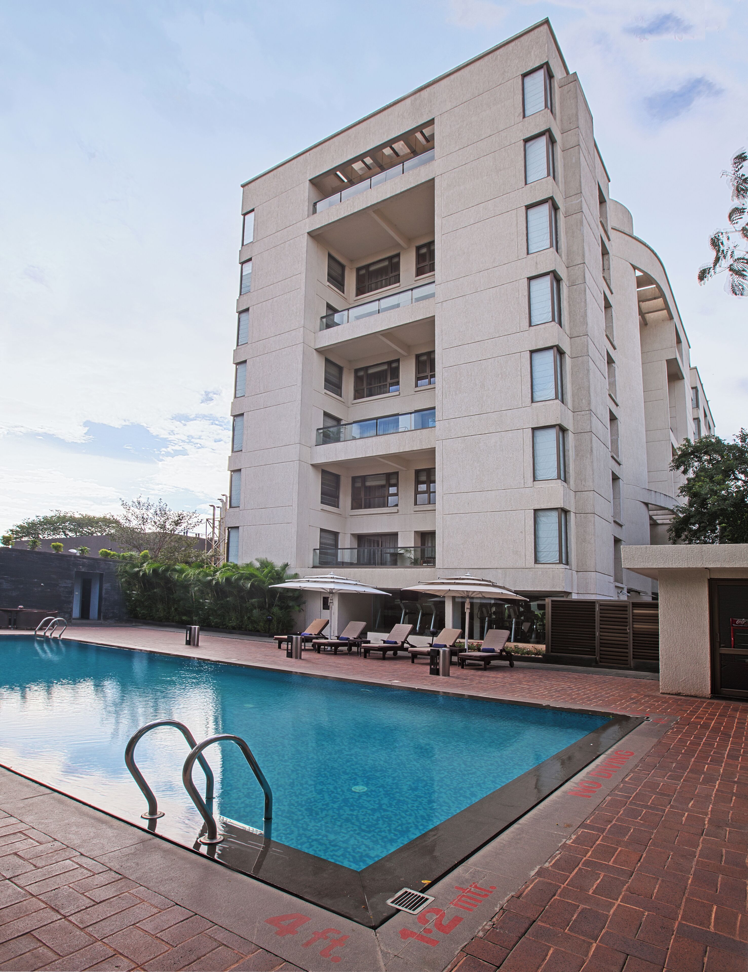 A multi-story hotel with a swimming pool, outdoor seating, and a clear sky.