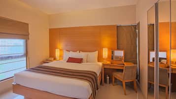 Una habitación de hotel con una cama grande, un escritorio con una silla, una computadora y un espejo.
