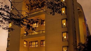 Un hotel de varios pisos con zona de piscina, mobiliario exterior e iluminación destacada en la fachada.