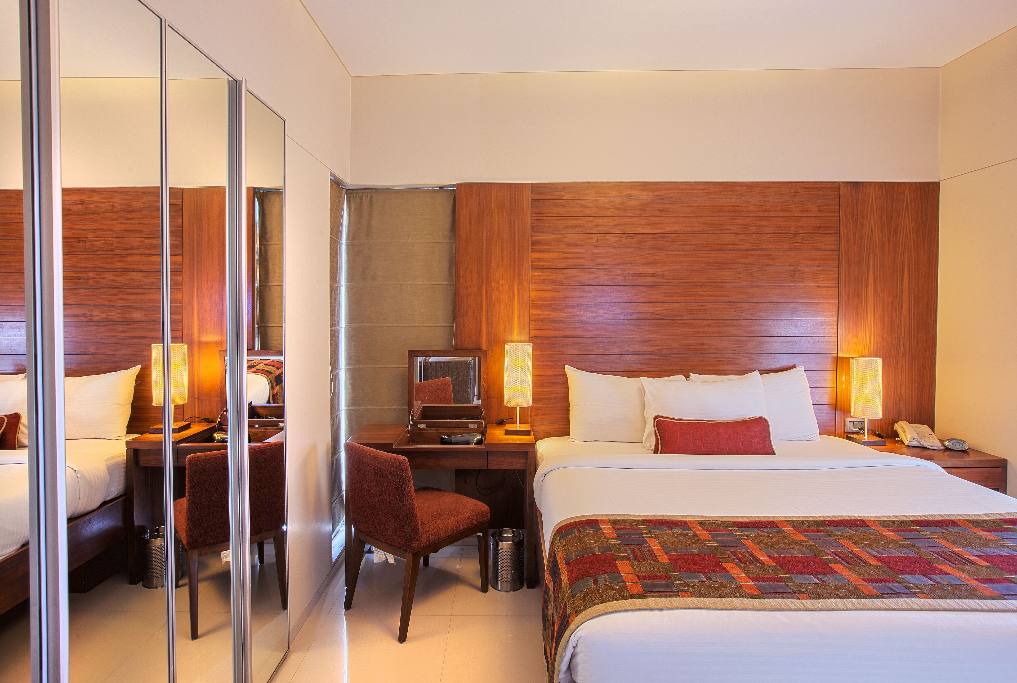 A hotel room with a bed, desk, chair, and a mirror.