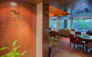Un restaurante con una pared de madera que presenta un logotipo de hoja y el nombre "Oakleaf". En su interior, hay mesas y sillas de madera, un sofá y un amplio ventanal con vistas al exterior.