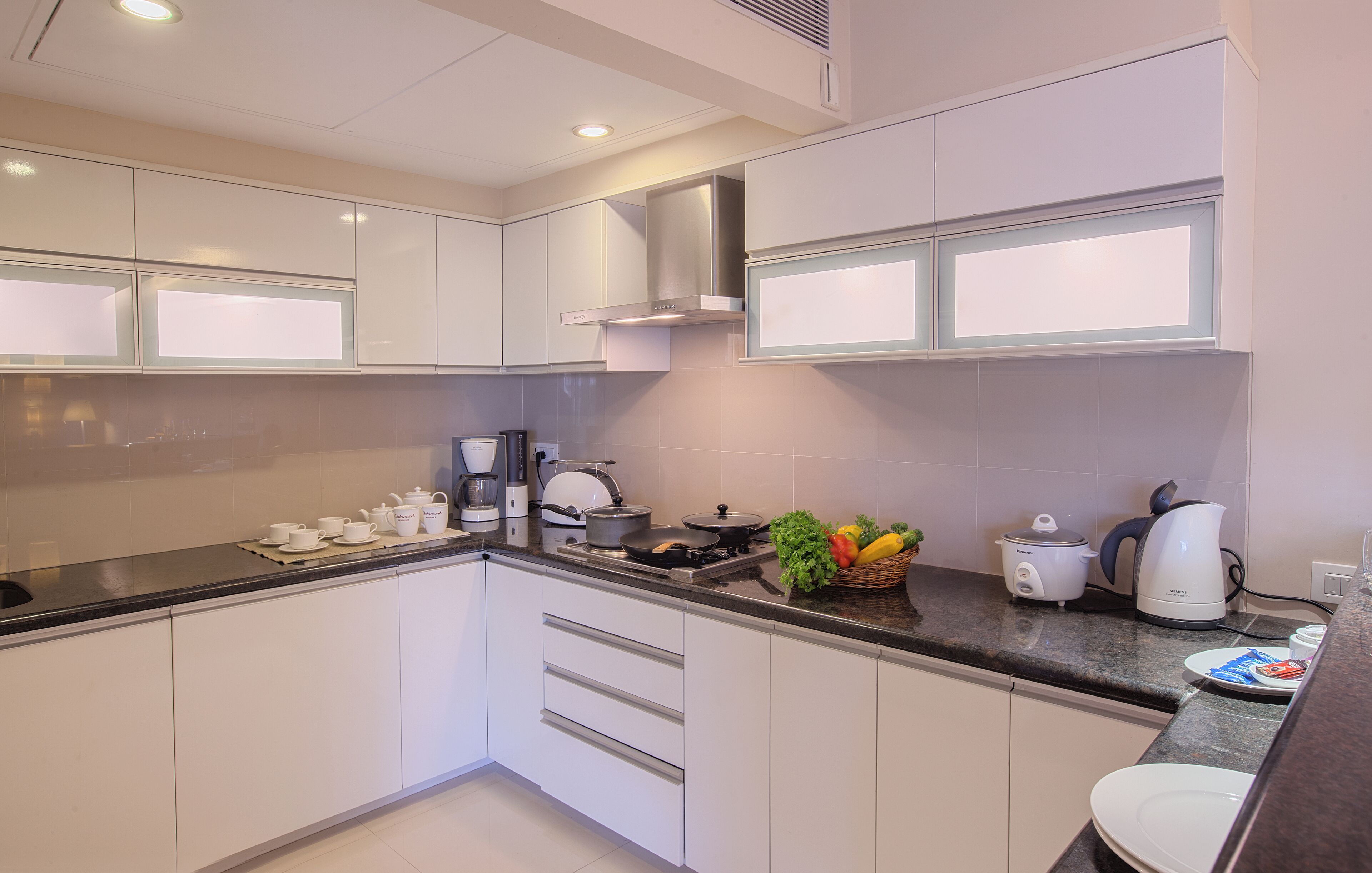 A modern kitchen with white cabinets, a stove, a coffee maker, and a fruit basket.