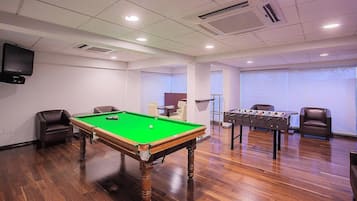 A room with a pool table, a foosball table, and a television.